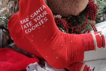 Person wearing red socks that read "Dear Santa, I ate your cookies" next to a plate of cookies.