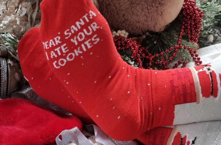 Person wearing red socks that read "Dear Santa, I ate your cookies" next to a plate of cookies.