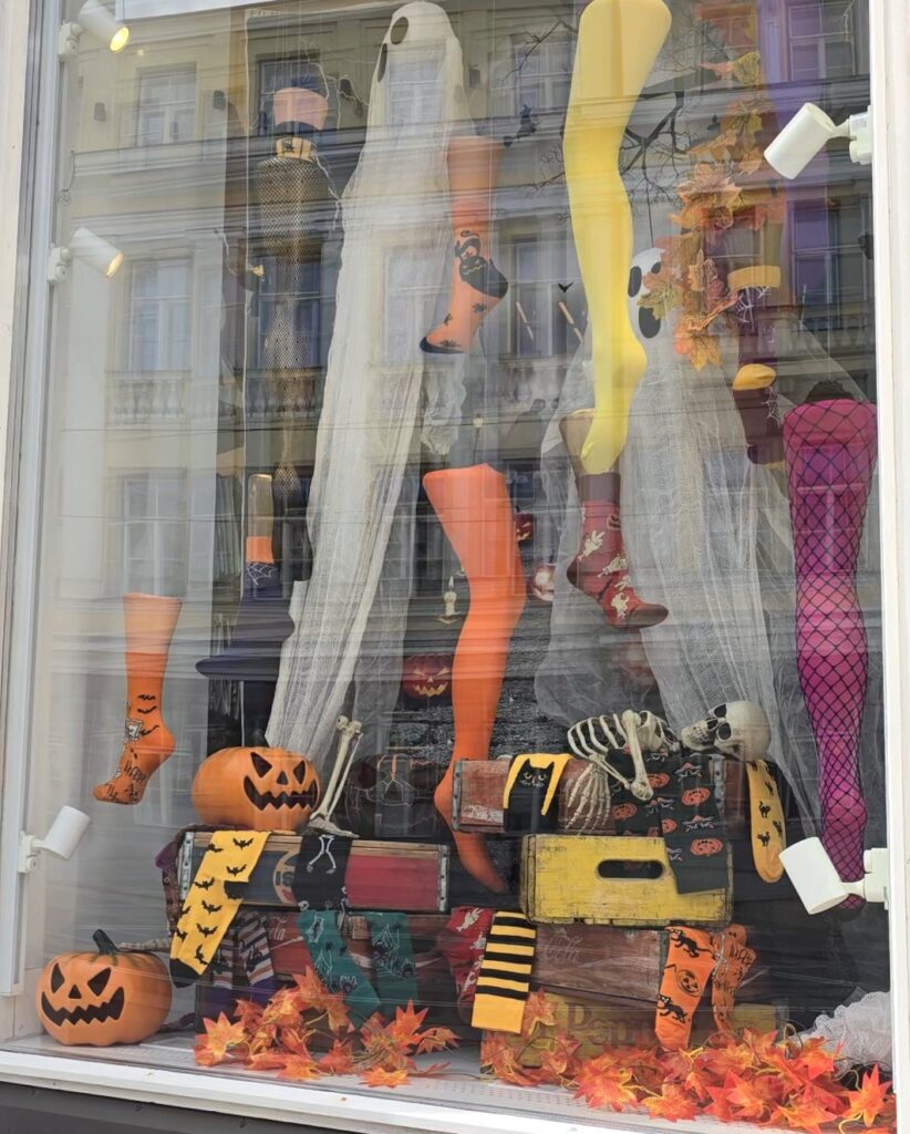 Halloween window display featuring pumpkins, artificial trees, and spooky Halloween decorations.