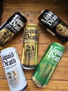 Cans of Liquid Death water and flavored sparkling water varieties on a wooden surface.