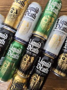 Stacked cans of Liquid Death water and sparkling water varieties on a wooden surface.