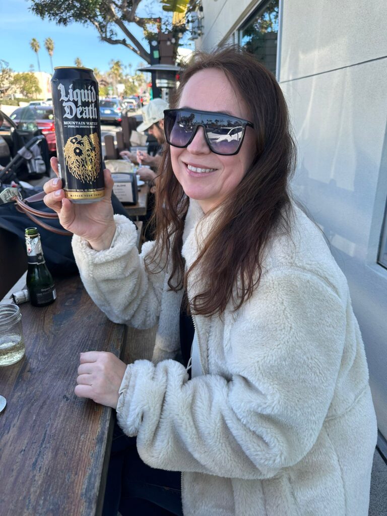 Author holding a can of "Liquid Death" mountain water at an outdoor café