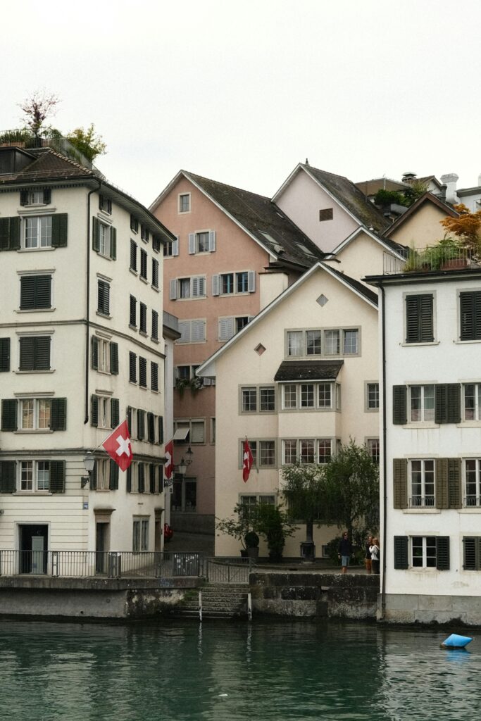 Charming Swiss buildings with Swiss flags along a serene riverside, showcasing traditional architecture and a peaceful atmosphere.