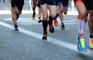 Close-up of runners' legs and feet in a marathon or race, showing various types of running shoes on the asphalt.