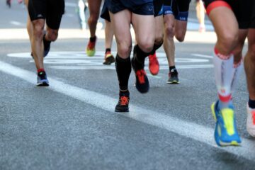 Close-up of runners' legs and feet in a marathon or race, showing various types of running shoes on the asphalt.