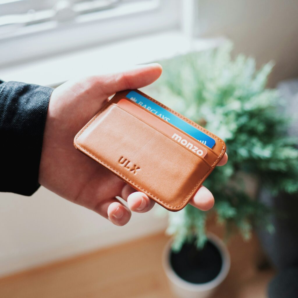 Hand holding a wallet with a Monzo card and a Barclays card inside.