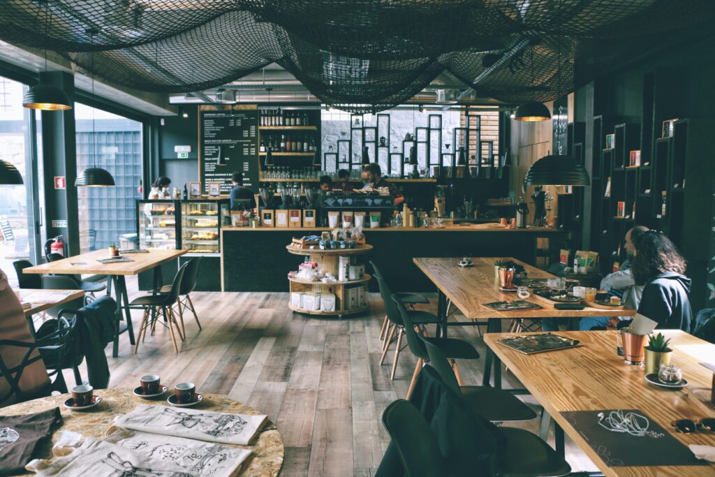 Modern, industrial café interior with wooden floors, black mesh ceiling, dark furniture, and a well-stocked coffee bar in the background.