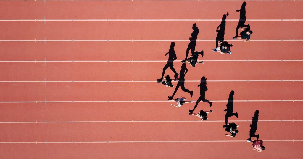 Aerial view of runners' shadows on a red athletic track, illustrating competition and growth in the running market.