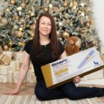 Vanessa sitting near a decorated Christmas tree holding a large box of Ozempic (semaglutide) injection.